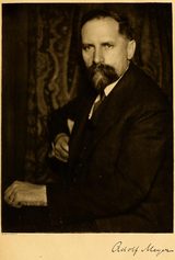 Sepia photograph of Adolf Meyer, a man with dark hair, a mustache and a full pointed beard, seated in a dark suit with one hand resting on a book; his signature is printed below.